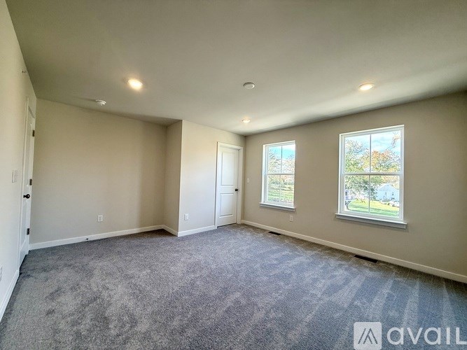 A spacious room with a carpeted floor and two windows.