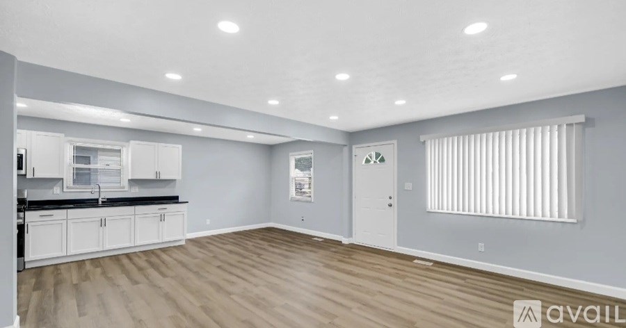 A spacious kitchen and living room with wooden flooring and white cabinetry.