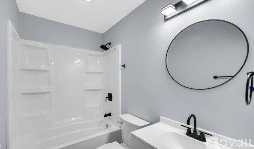 A white bathroom with a round mirror and a white bathtub.