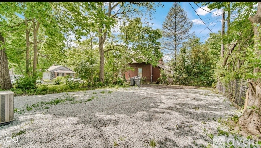 A gravel driveway leads to a small house surrounded by trees.