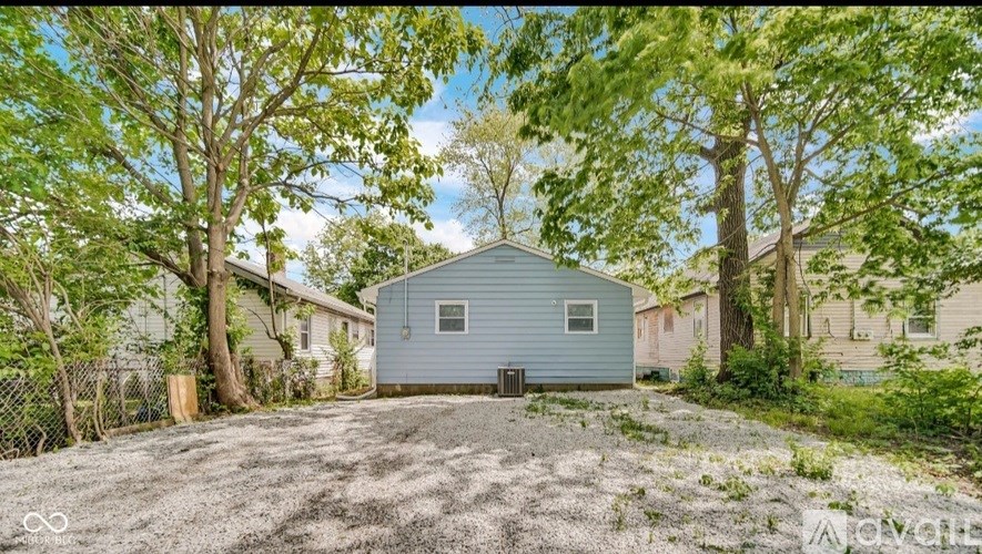 A blue shed sits in the middle of a gravel area with trees in the background.