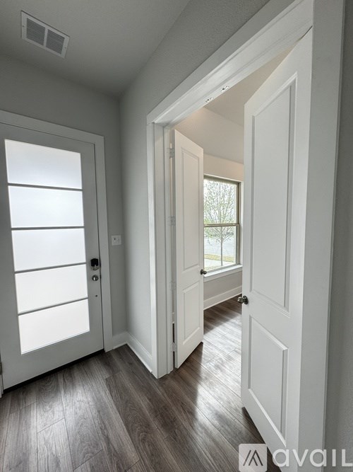 A white door is open to a hallway with wood flooring.