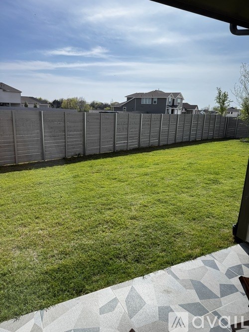A backyard with a grey fence and a green lawn.