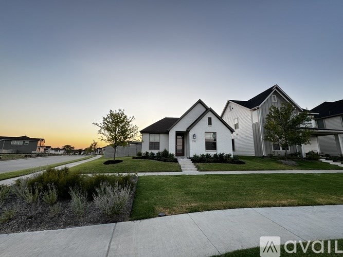 A house with a white exterior is surrounded by a well-kept lawn and a sidewalk.