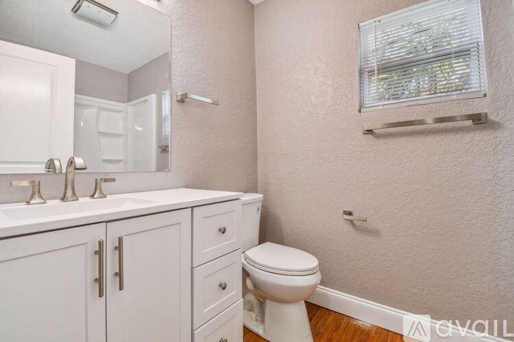 A white toilet sits in a bathroom with a white sink and a window.