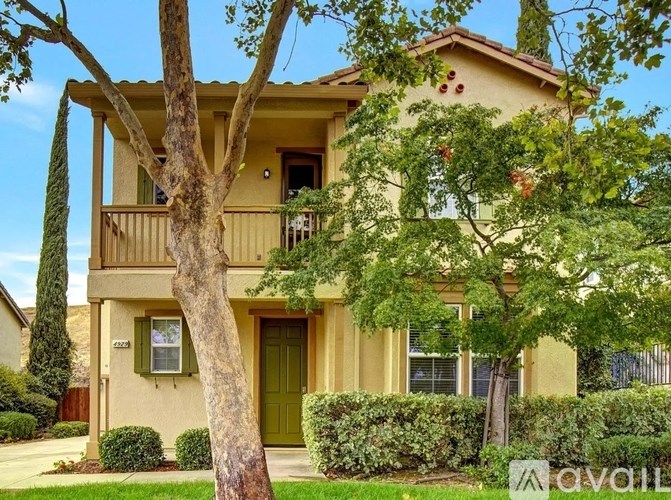 A beige two-story house with a green door and a tree in front.