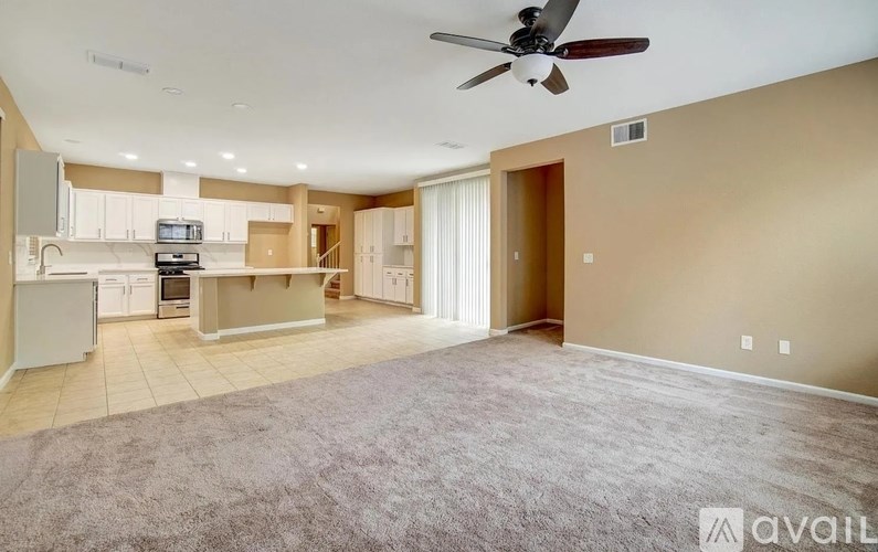 A spacious living room with a ceiling fan and a carpeted floor.