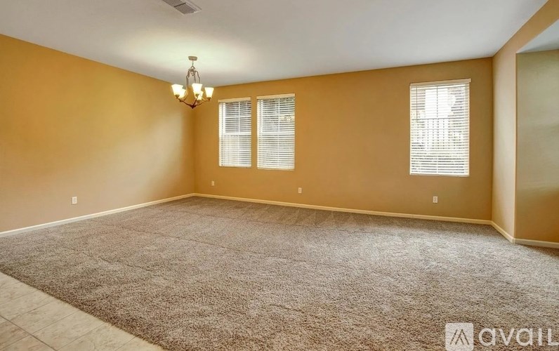 A room with a carpeted floor, a ceiling fan, and two windows with blinds.