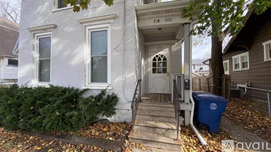 A house with a blue trash bin in front of it.