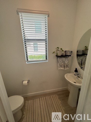 A bathroom with a toilet, sink, and window with blinds.
