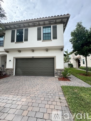 A white house with a grey garage door and a brick driveway.