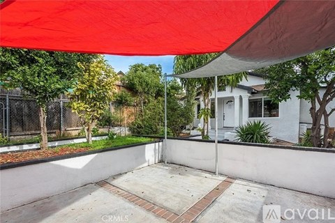 A red canopy is over a white house and a white fence.