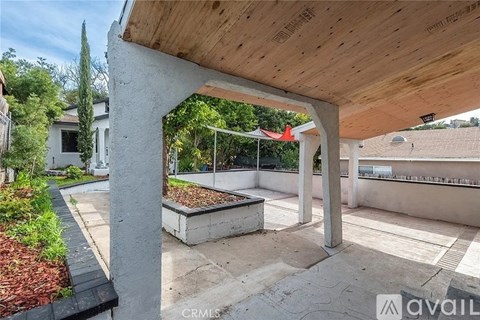 A wooden pergola with a red umbrella is in the middle of a concrete patio.