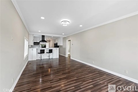 A spacious room with wooden flooring and a kitchen area in the background.