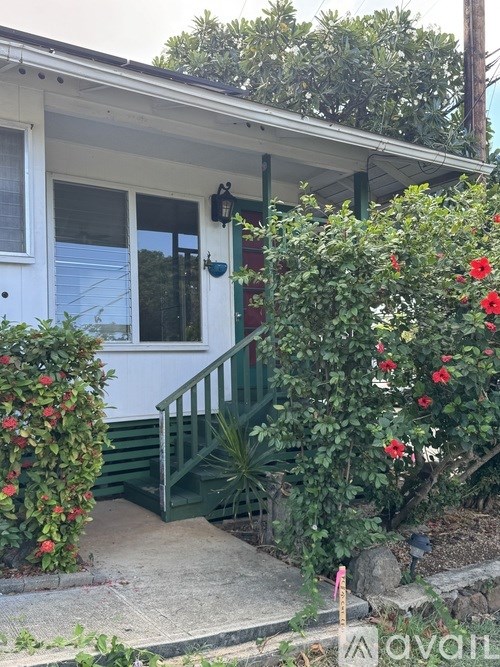A white house with a green staircase and red flowers.