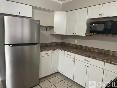 A kitchen with a stainless steel refrigerator, white cabinets, and a granite countertop.