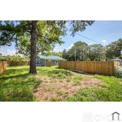 A backyard with a fence, a tree, and a house in the background.
