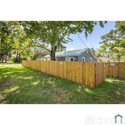 A wooden fence in front of a house with trees in the background.