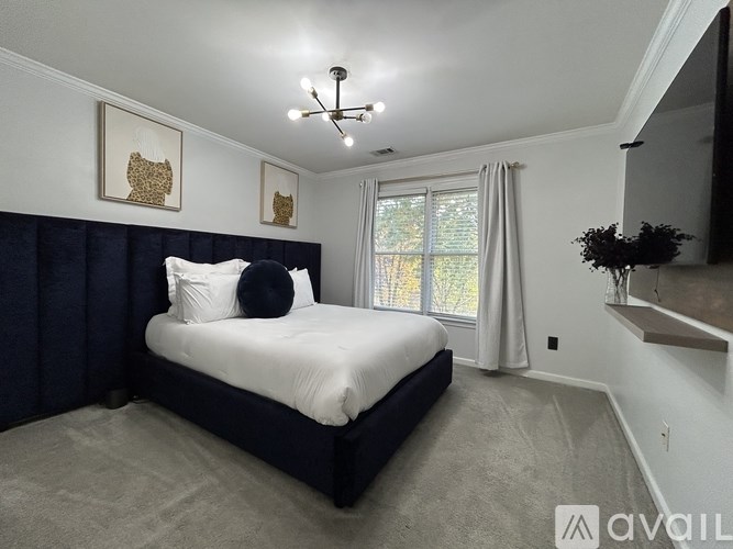 A bedroom with a large bed and a window with white curtains.