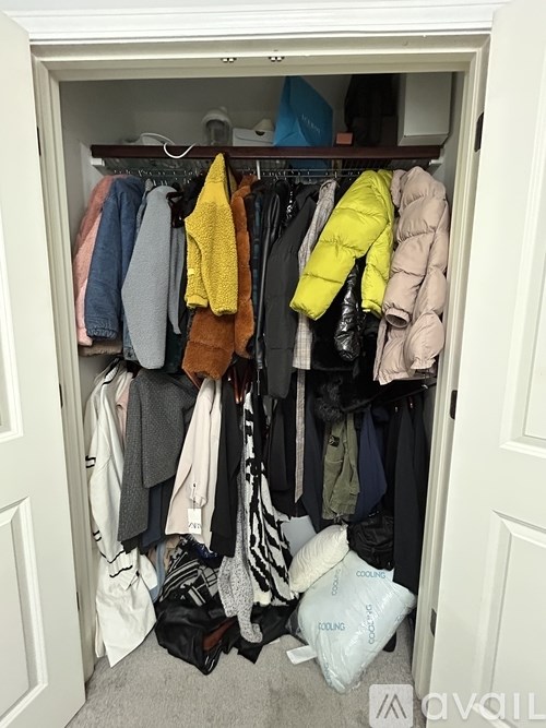 A white closet with clothes hanging and bags on the floor.