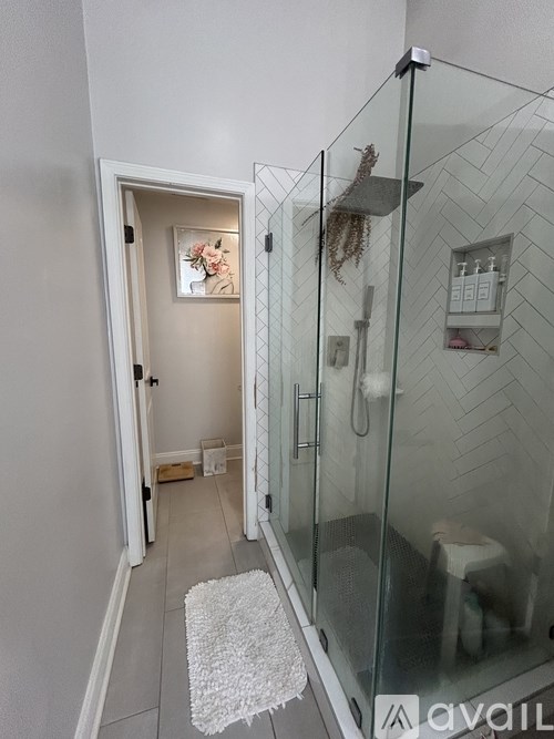 A bathroom with a glass shower enclosure and a white rug on the floor.