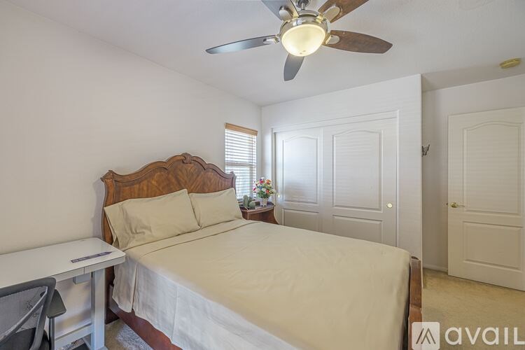 A bedroom with a bed, desk, and fan.