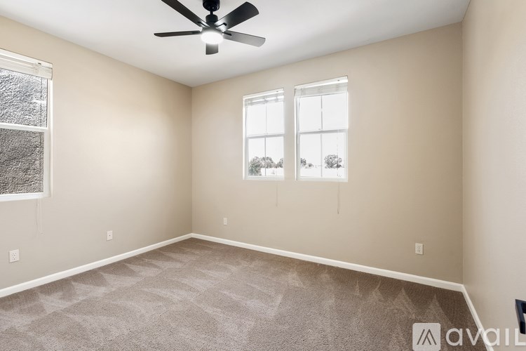 A room with a ceiling fan, two windows, and carpeted floor.