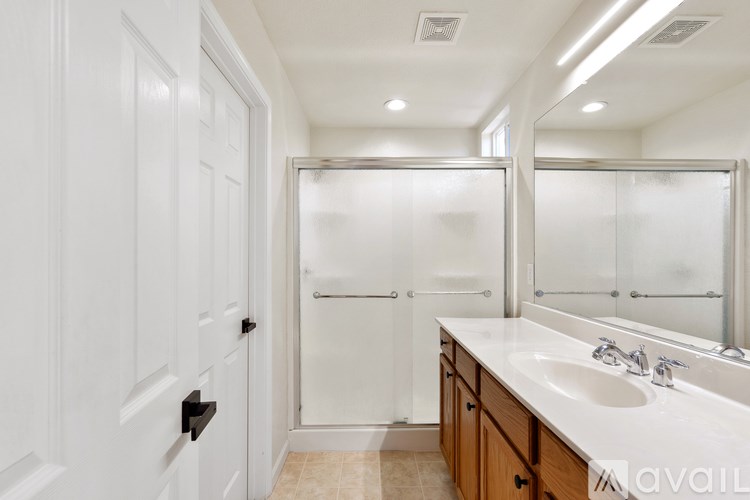 A bathroom with a white door, a glass shower, and a sink with a mirror above it.