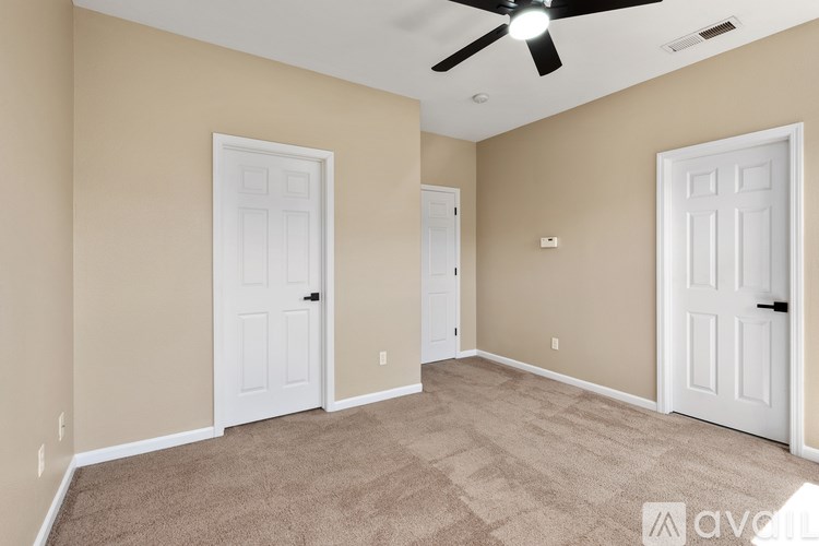 A room with beige walls and carpet flooring, featuring a ceiling fan and two white doors.