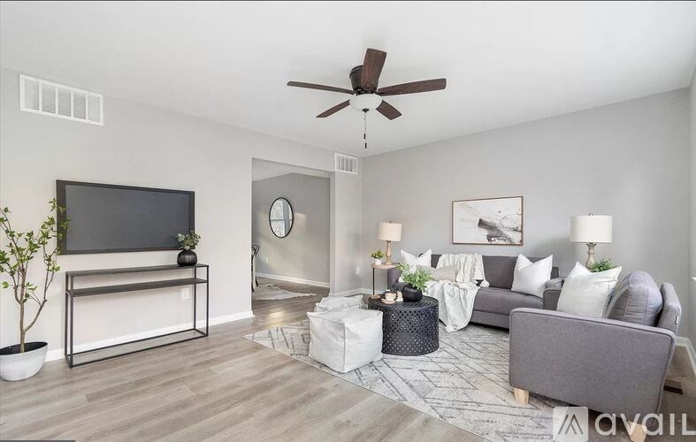 A living room with a grey couch, a white coffee table, a flat screen TV, and a ceiling fan.