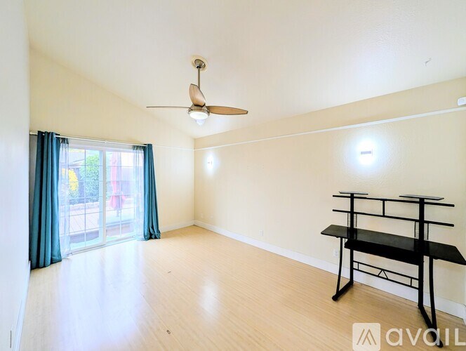 A room with a ceiling fan, a table, and a window with curtains.