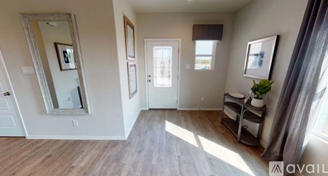 A room with a wooden floor and white walls, with a mirror, a door, and a plant on a shelf.