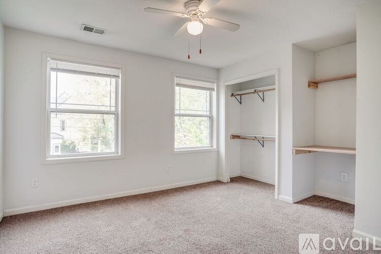 A room with a carpeted floor, a ceiling fan, and two windows.