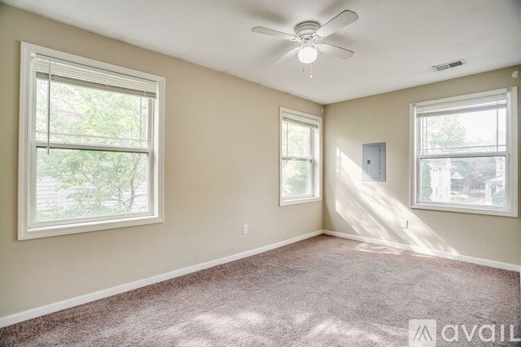 A room with a carpeted floor, a ceiling fan, and three windows.