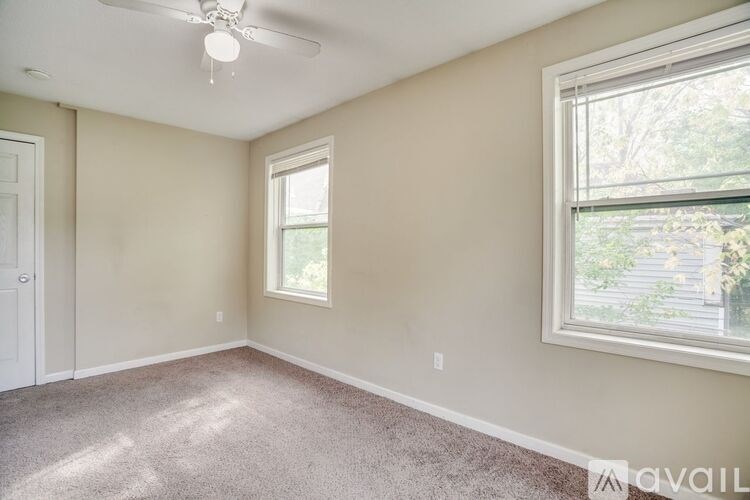 A room with a carpeted floor, a ceiling fan, and two windows.