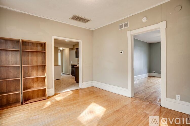 A room with wooden floors and a large open doorway leading to another room.