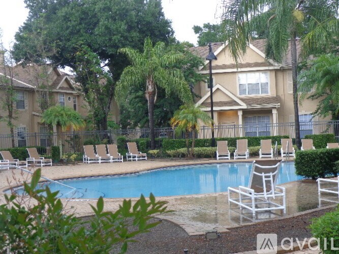 A pool surrounded by chairs and trees in front of a house.