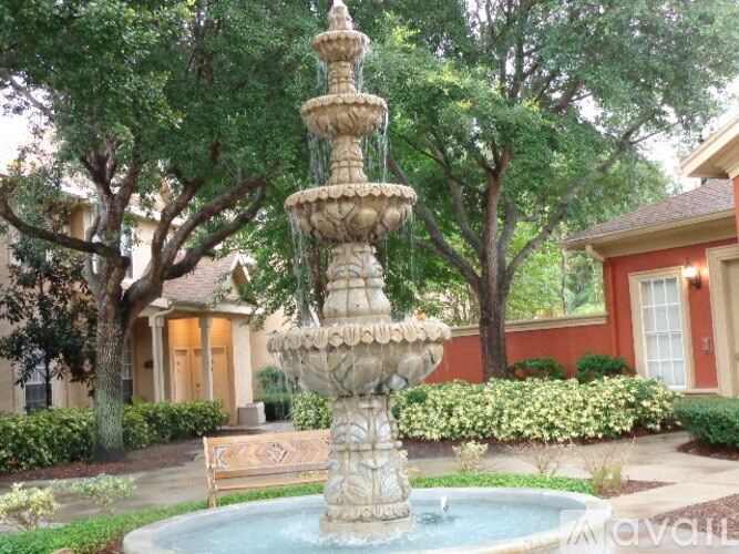 A fountain in the middle of a garden with a bench in front of it.