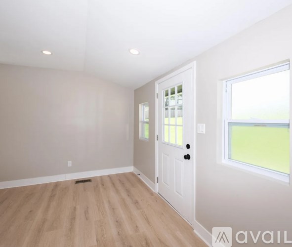 A room with a white door and a window with a view of a green field.