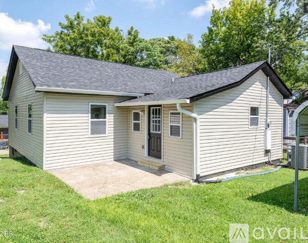 A small house with a grey roof and a white exterior is surrounded by a grassy area.