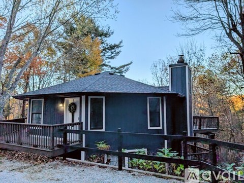 A small house with a porch and a chimney is surrounded by trees.