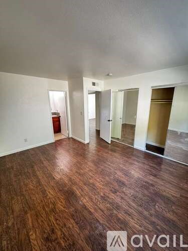 A room with wooden floors and white walls, with a door on the left and three other doors in the background.