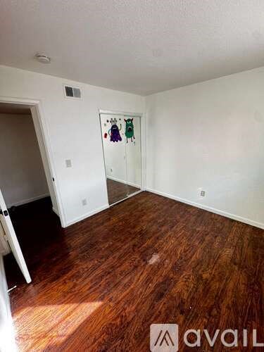 A room with wood flooring and a white wall with a picture hanging on it.