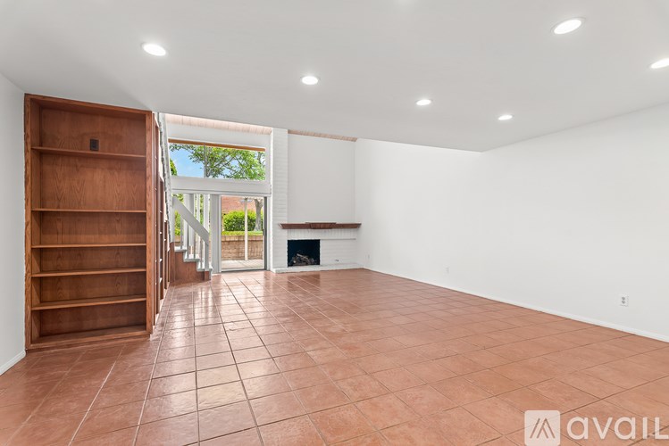 A room with a tiled floor and a fireplace with a view of a garden outside.