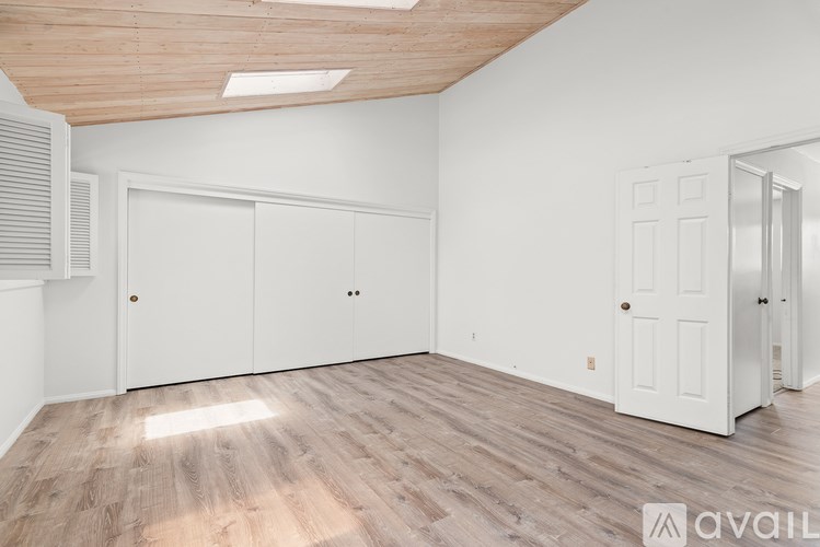 A room with white walls and wooden flooring, with a skylight above and two white doors.