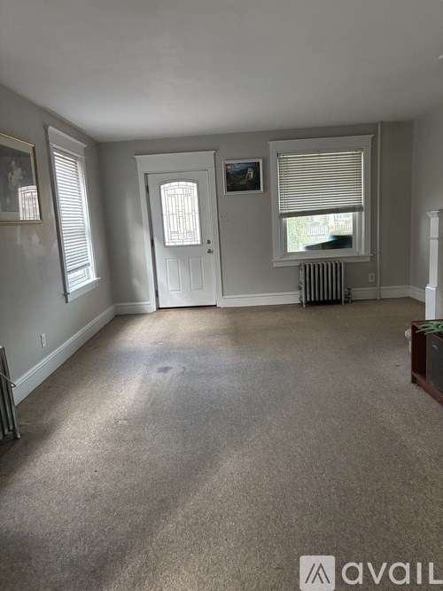 A room with a carpeted floor, a white door, and a window with blinds.