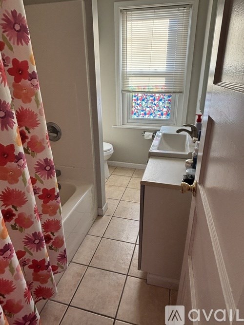 A bathroom with a floral shower curtain and a window with a floral valance.