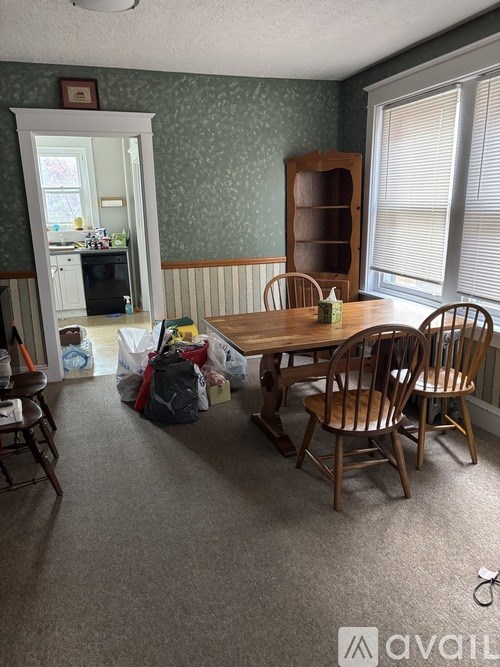 A room with a dining table and chairs, a bookshelf, and a pile of boxes on the floor.