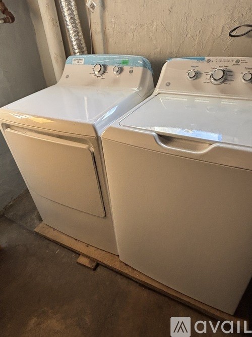 Two white washing machines are sitting on a wooden pallet.