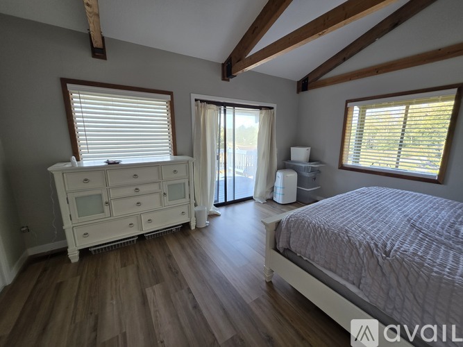 A bedroom with a large bed, a dresser with a mirror, and a window with blinds.